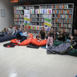 Dziewczęta siedzą na pufach i materacach przed regałem z książkami