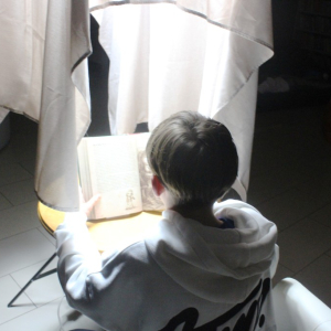 Chłopiec czyta pod lampą osłoniętą szalem