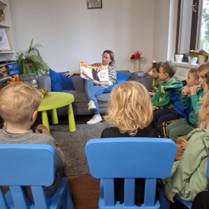 Grupa dzieci słucha opowiadania czytanego przez bibliotekarkę