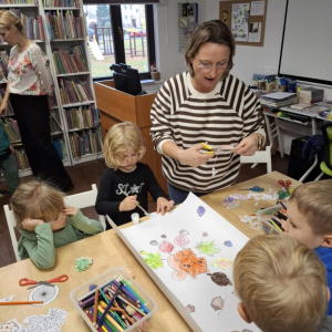 Kilkoro dzieci pod okiem bibliotekarki tworzy jesienną mandalę