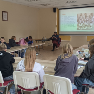 Uczestnicy siedzą przy sołe ustawionym w podkowę i oglądaja prezentację