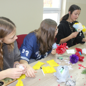 Trzy dziewczyny przy stole tworzą kwity z bibuły