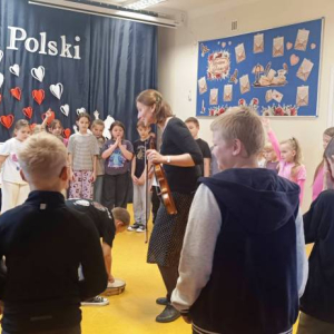 Dzieci stoją w okręgu, prowadząca stoi po środku koła.