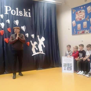 Mężczyzna mówi do dzieci siedzących na ławkach.