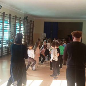 Kobieta i mężczyzna stoją przed dziećmi, które dopingują biegnącą pare w trakcie zabawy