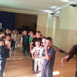 Dzieci stoja w szpalerze obserwując mężczyznę goniącego kobietę