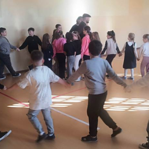 Chłopcy i dziewczynki oraz prowadzący trzymają się za ręce w korowodzie 