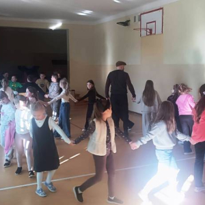 Chłopcy i dziewczynki oraz prowadzący trzymają się za ręce w korowodzie 