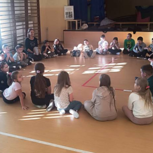 Dzieci i prowadzący siedzą w okręgu na podłodze