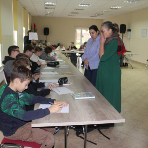 Dwie kobiety rozmawiają stoją przed uczniami siedzącymi przy stole.