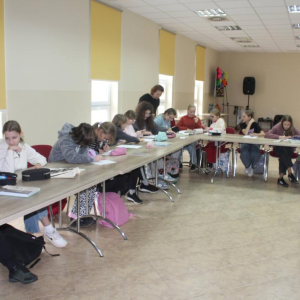 Młodzież siedzi przy stołach pisząc