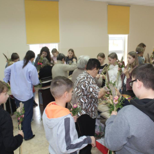 Grupa uczestniów stoi wokół stołów układając palmy