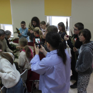 Uczestnicy stoją w grupie przy stołach pracując na palmami