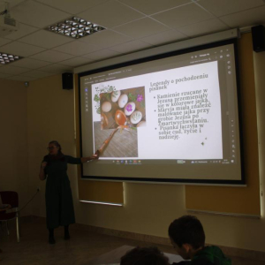 Kobieta przy ekranie z prezentacją wskazuje na slajd