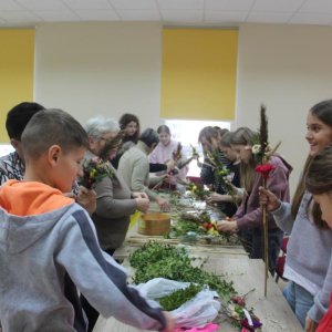 Młodzież stoi wokół stołu z materiałmi na palmy wielkanocne