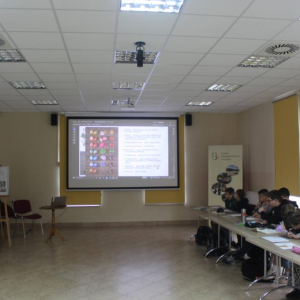 Grupa uczniów siedzi przy stołach oglądając prezentację