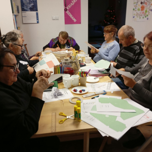 Seniorzy na spotkaniu w bibliotece wycinają i kleją papierowe dekoracje 