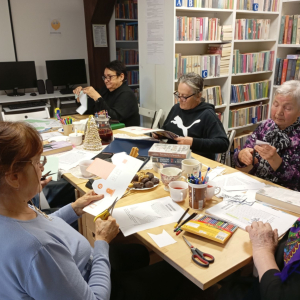 Seniorzy na spotkaniu w bibliotece wycinają i kleją papierowe dekoracje 