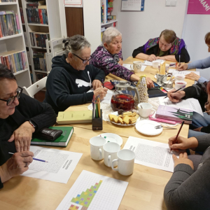 Seniorzy na spotkaniu w bibliotece wycinają i kleją papierowe dekoracje 