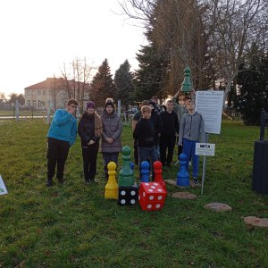 Na pierwszym planie widoczne pionki gry terenowej, a w tle grupa młodzieży śledząca rozgrywkę.