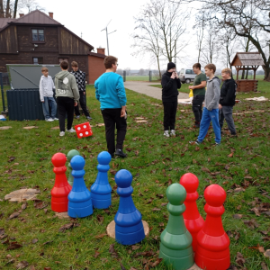 Na pierwszym planie widoczne pionki gry terenowej, a w tle grupa młodzieży śledząca rozgrywkę.