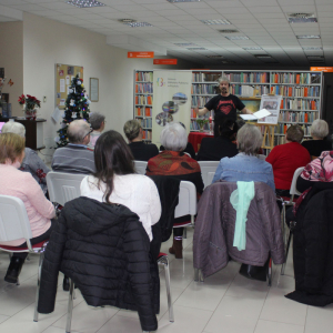Publiczność zgromadzona w bibliotece słucha autora, który prezentuje swoje utwory poetyckie podczas recitalu.