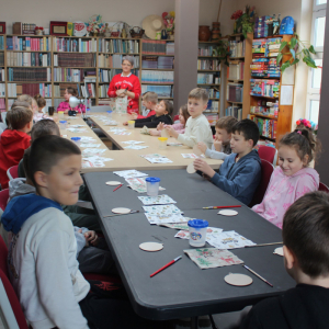 Dzieci siedzą przy stole i zaczynają warsztaty decoupage podczas bożonarodzeniowego spotkania w bibliotece.