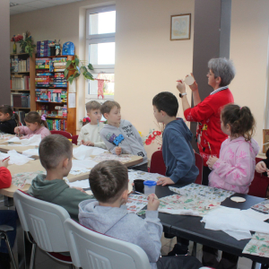  Pani Edyta pokazuje dzieciom, jak prawidłowo wykonać ozdobę na bombce metodą decoupage podczas warsztatów w bibliotece.