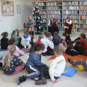 Dzieci wraz z paniami z Koła Gospodyń Wiejskich obserwują Panią Janinę, która gra na skrzypcach podczas bożonarodzeniowego spotkania w bibliotece.