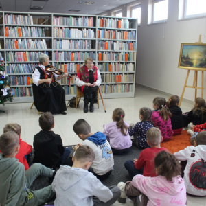  Dzieci wraz z paniami z Koła Gospodyń Wiejskich obserwują Panią Janinę, która gra na skrzypcach podczas bożonarodzeniowego spotkania w bibliotece.