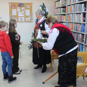  Dzieci wręczają bożonarodzeniowy stroik paniom z Koła Gospodyń Wiejskich podczas świątecznego spotkania w bibliotece.