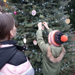 Dziewczynka i chłopiec wieszają ozdoby na choince