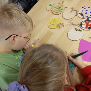 Dwoje dzieci koloruje drewniane bombki