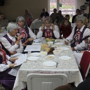 Kobiety w strojach ludowych siedzą wokól stołu.