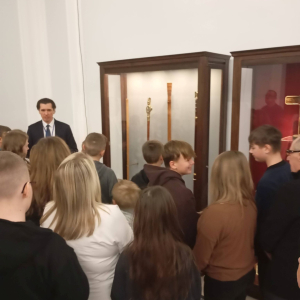 Grupa uczestników z przewodnikiem przy gablocie z laskami marszałkowskimi.