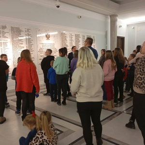 Przewodnik omawia grupie zwiedzających tablicę poświęconą parlamentarzystom poległym podczas II wojny światowej.