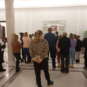 Przewodnik omawia grupie zwiedzających tablicę poświęconą tym, którzy zginęli w katastrofie pod Smoleńskiem.