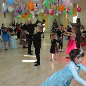 Dzieci w kostiumach karnawałowych tańczą w parach w udekorowanej sali.