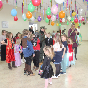 Dzieci w kostiumach bawiące się w sali udekorowanej kolorowymi balonami i wstążkami.