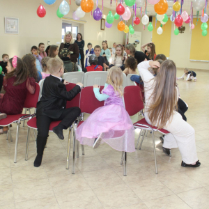 Dzieci siedzące na krzesłach w rzędzie podczas zabawy w sali z balonami.