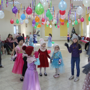 Grupa dzieci w zimowych czapkach i kostiumach podczas zabawy tanecznej.