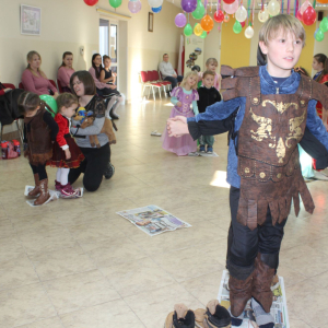 Chłopiec w zbroi rycerskiej stoi na gazecie podczas zabawy zręcznościowej w udekorowanej sali.