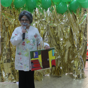 Dziewczynka w stroju malarza trzymająca w dłoniach obraz.