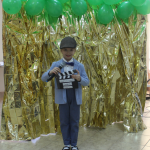 Dziewczynka w kaszkiecie z klapsem filmowym i mikrofonem na złotym tle.