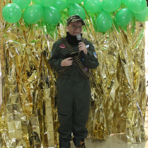 Chłopiec w stroju żołnierza z mikrofonem na tle złotej kurtyny.