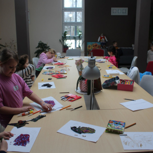 Dzieci wykonujące prace plastyczne przy stole w bibliotece.