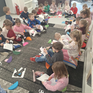 Dzieci siedzą na dywanie i wycinają z papieru.