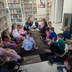 Uczestnicy zajęć siedzą w okręgu ,słuchają bibliotekarki.