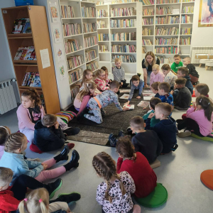 Dzieci siedzą na dywanie w okręgu , rozwiązują zadania wspólnie z prowadzącą zajęcia.