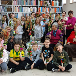 Uczesnicy warsztatów wielkanocnych wraz z prowadzącymi pozują do zdjęcia,trzymając w rękach samodzielnie wykonane palmy.